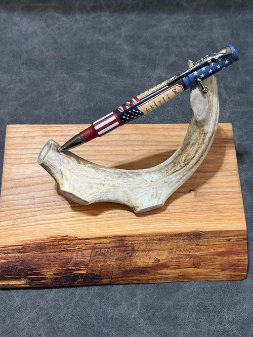 Handcrafted .30 caliber bolt action pen with red, white, and blue 2nd Amendment custom blank and chrome accents displayed on antler stand